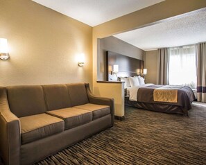 A hotel room with a brown sofa, a bed with a dark brown bedspread, a large mirror, and a window with curtains. - Quality Inn Dayton North - Vandalia (Dayton)