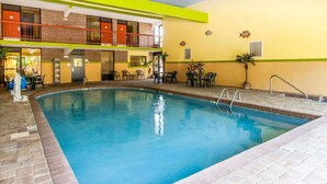 An indoor swimming pool with a brick border, a yellow and green wall, and a balcony with orange railings. - Quality Inn Sweetwater West (Sweetwater)