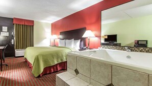 A hotel room with a bed, a desk, a chair, a large mirror, a television, and a bathtub. - Quality Inn Sweetwater West (Sweetwater)