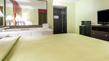 A hotel room with a bed, a television, a desk with a lamp, a mirror, and a door.