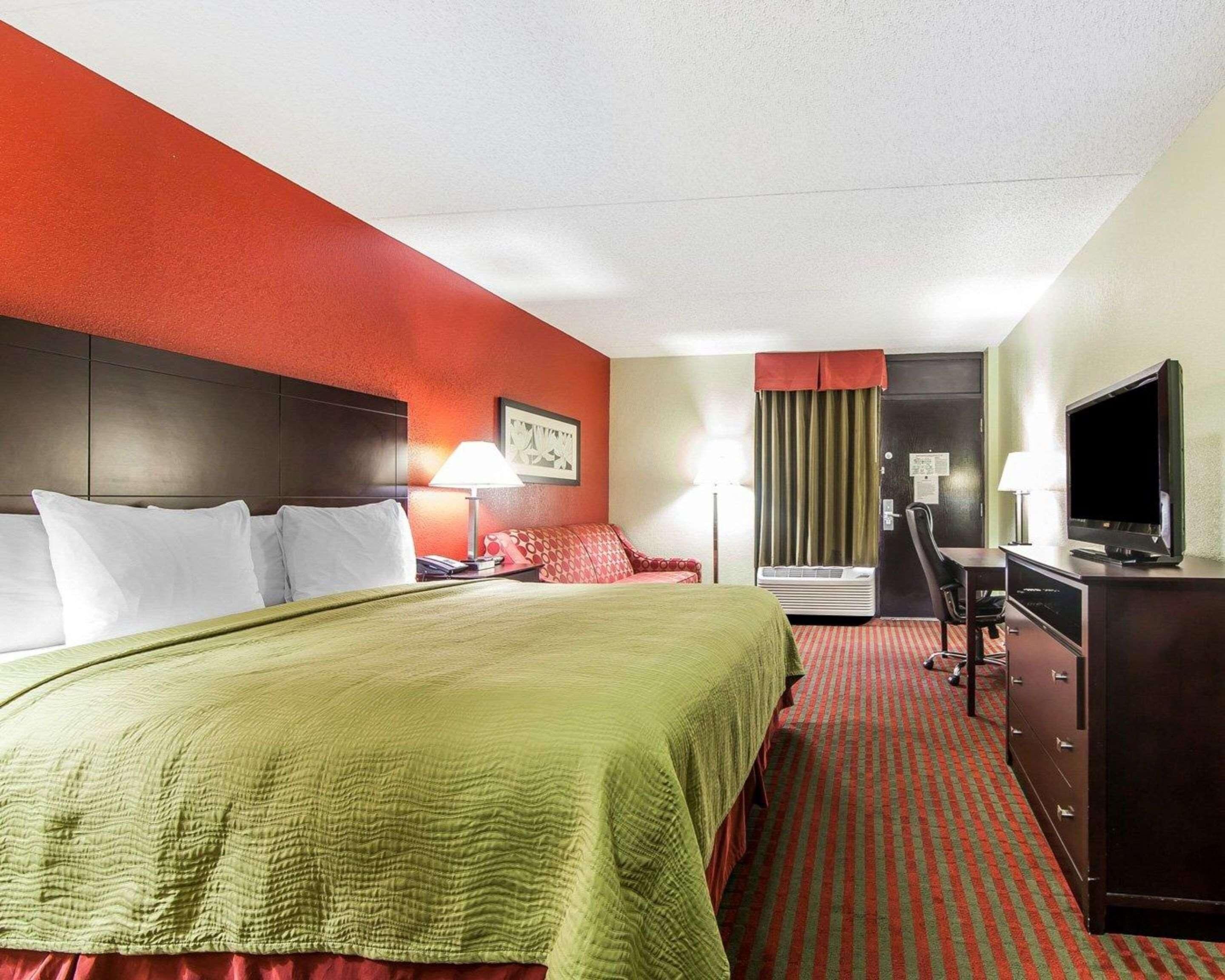 Habitación de hotel con cama, escritorio, televisión, silla y ventana con cortinas.