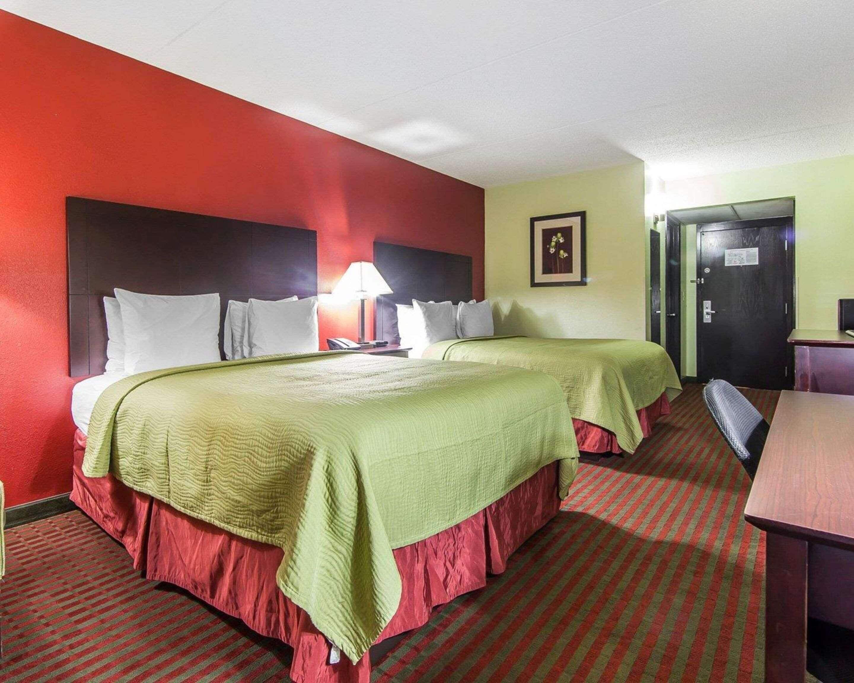 Una habitación de hotel con dos camas, un escritorio, una silla, una lámpara y una puerta.