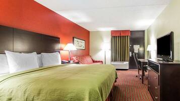 A hotel room with a large bed, a desk with a chair, a television, and a window with curtains.