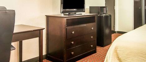 A hotel room with a bed, a desk with a television, a dresser, and a microwave.