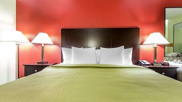 Quarto de hotel com uma cama grande, duas mesas de cabeceira com luminárias, uma parede de destaque vermelha e um edredom verde.