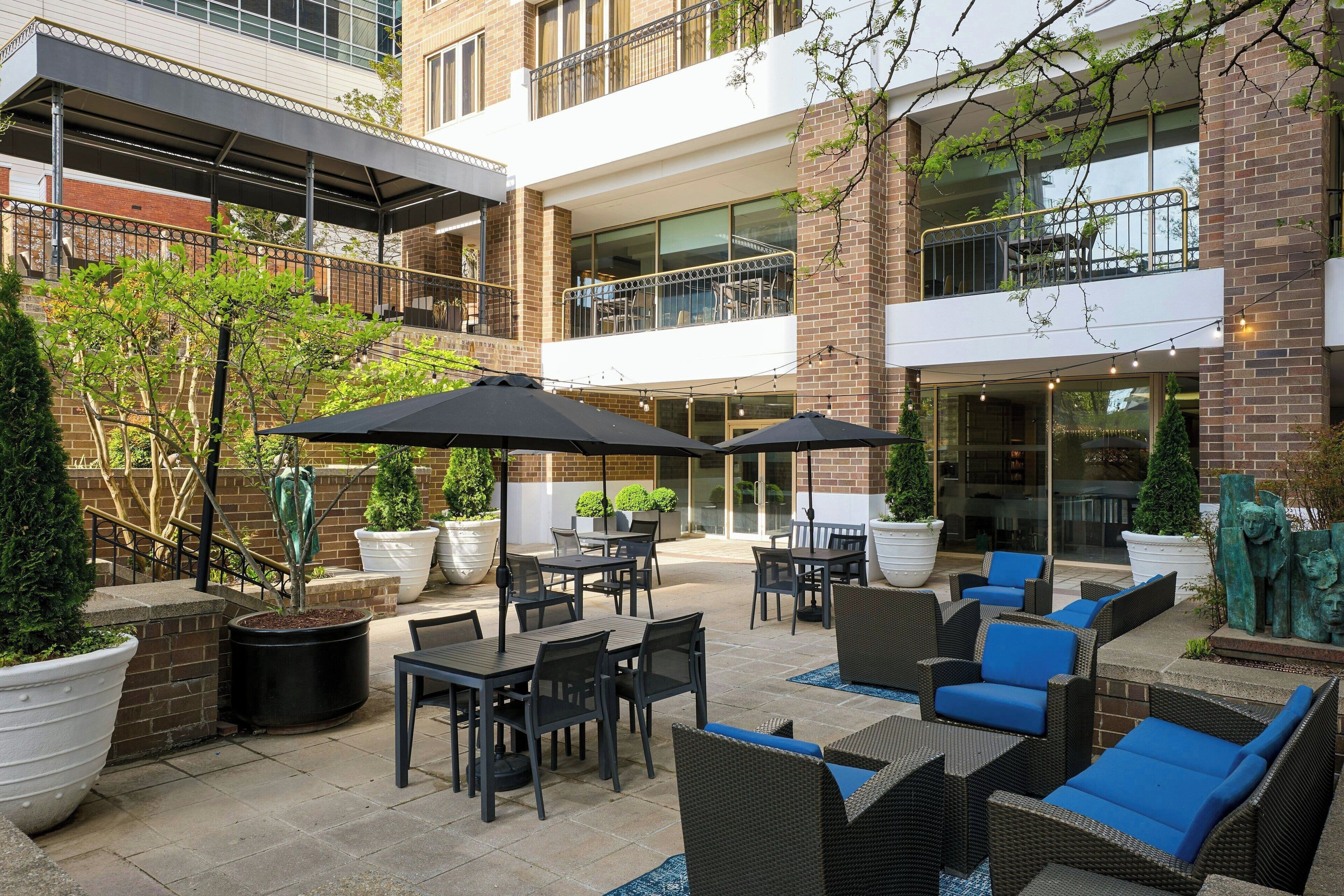 An outdoor patio area with tables and chairs, potted plants, and a covered seating area.