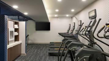 A fitness center with treadmills, a wall-mounted TV, and a small kitchenette area.