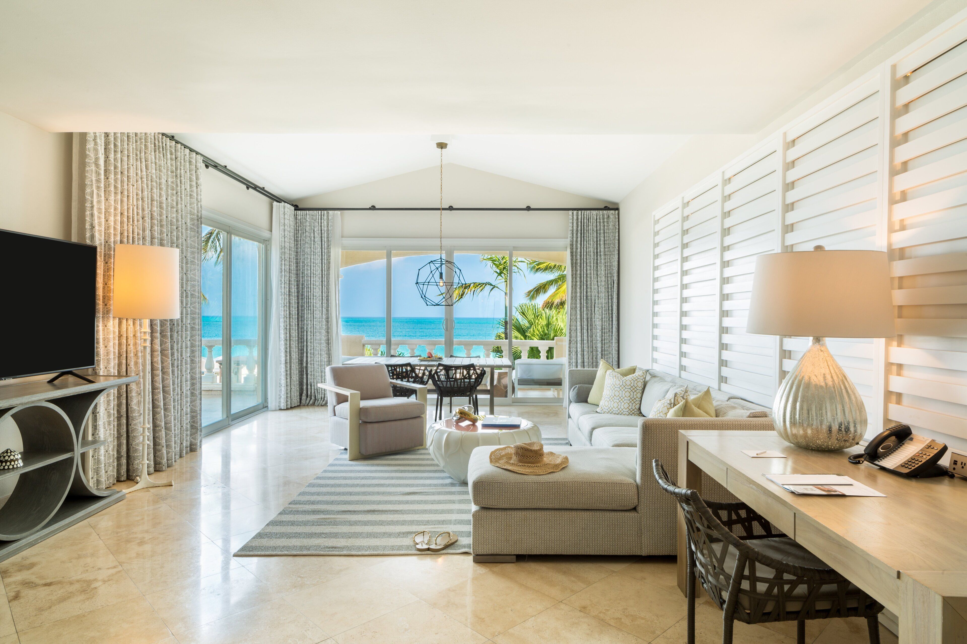 A spacious living room with a large TV, comfortable seating, a dining area, and a view of the ocean.