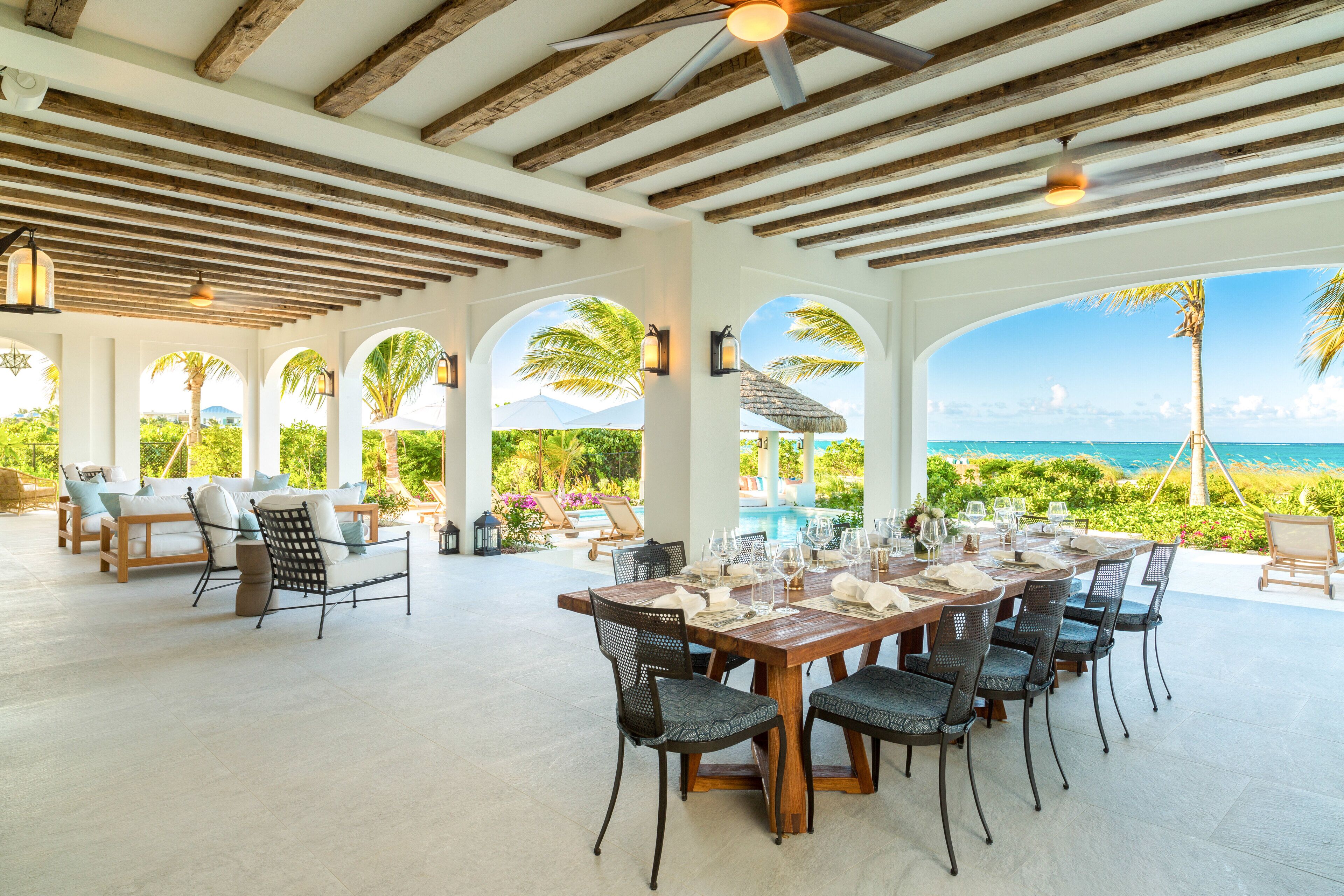 Amplia zona de comedor al aire libre con una mesa de madera dispuesta para seis personas, sillas alrededor y vistas al océano.