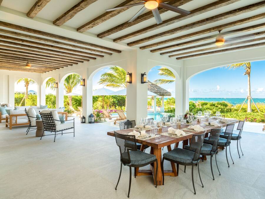 Amplia zona de comedor al aire libre con una mesa de madera dispuesta para seis personas, sillas alrededor y vistas al océano.