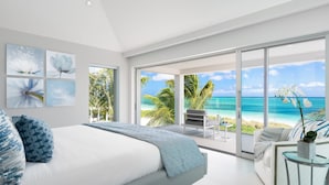 Un dormitorio moderno con una cama grande, un balcón con vista a la playa y un área de descanso con vista al océano.
