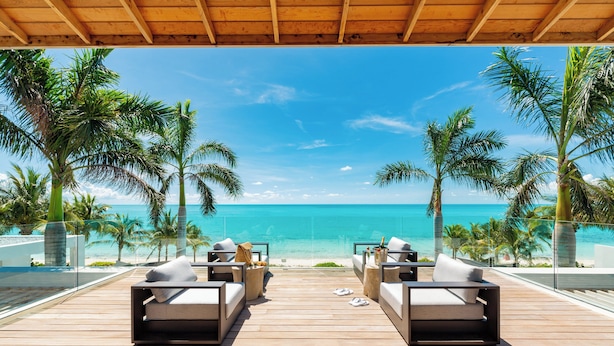 Una terraza de madera con sillones de descanso frente a la playa.