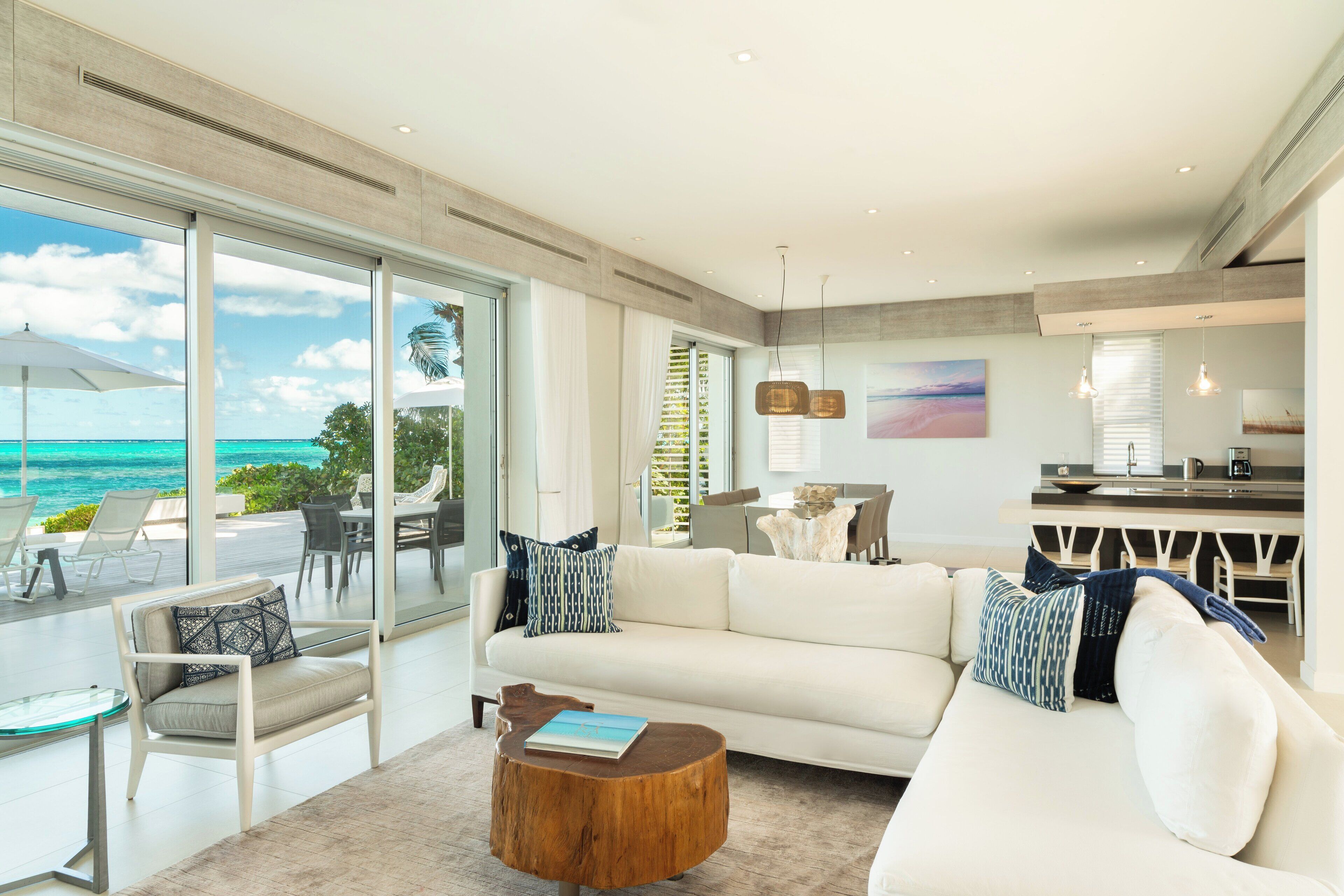 A spacious living area with a large window overlooking the ocean, a white sofa, a wooden coffee table, and a dining area with a view.