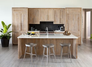 A modern kitchen with wooden cabinets, a central island with stools, a stove, and a sink.