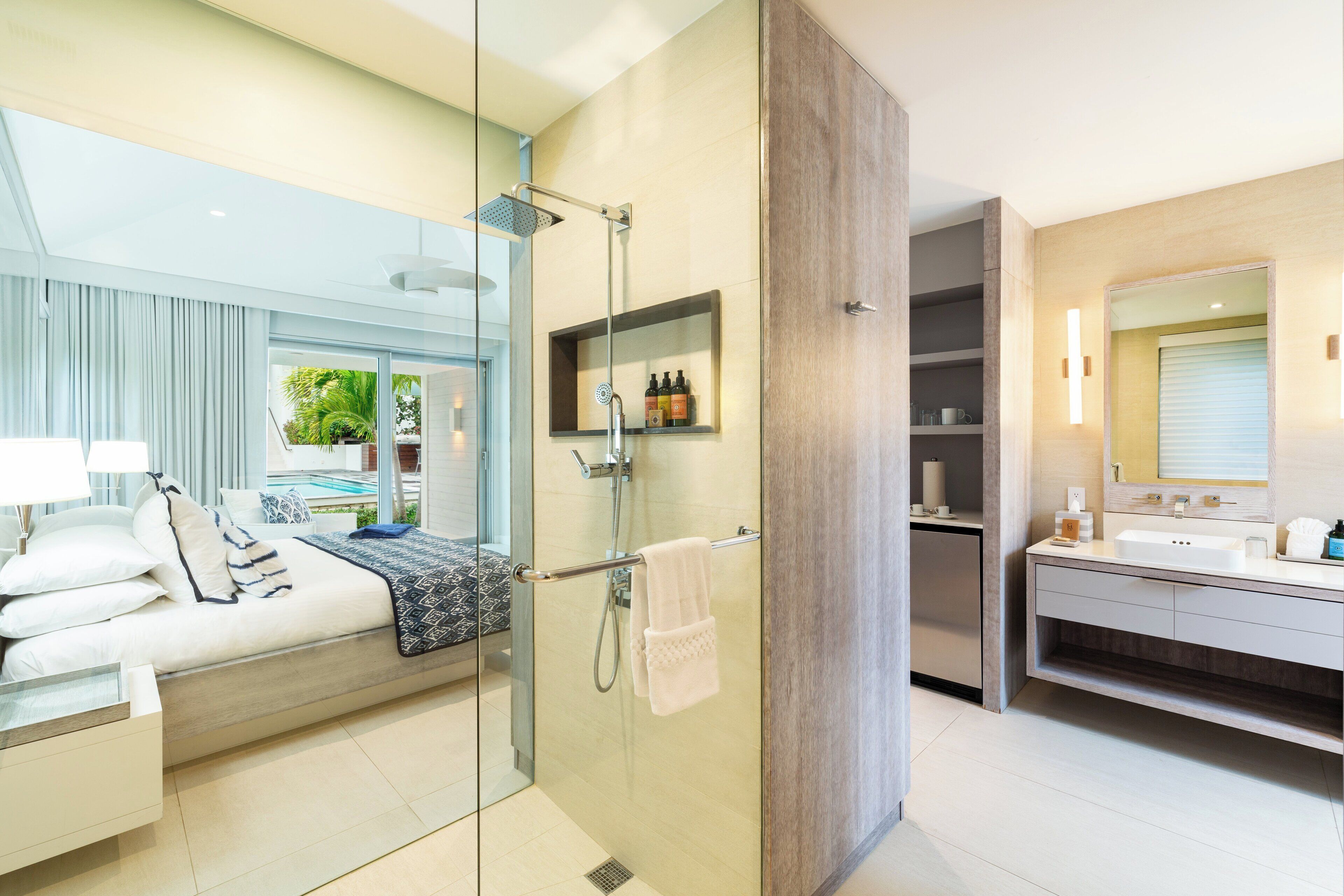Un baño moderno con ducha de vidrio, tocador con espejo y cama con vistas al exterior.