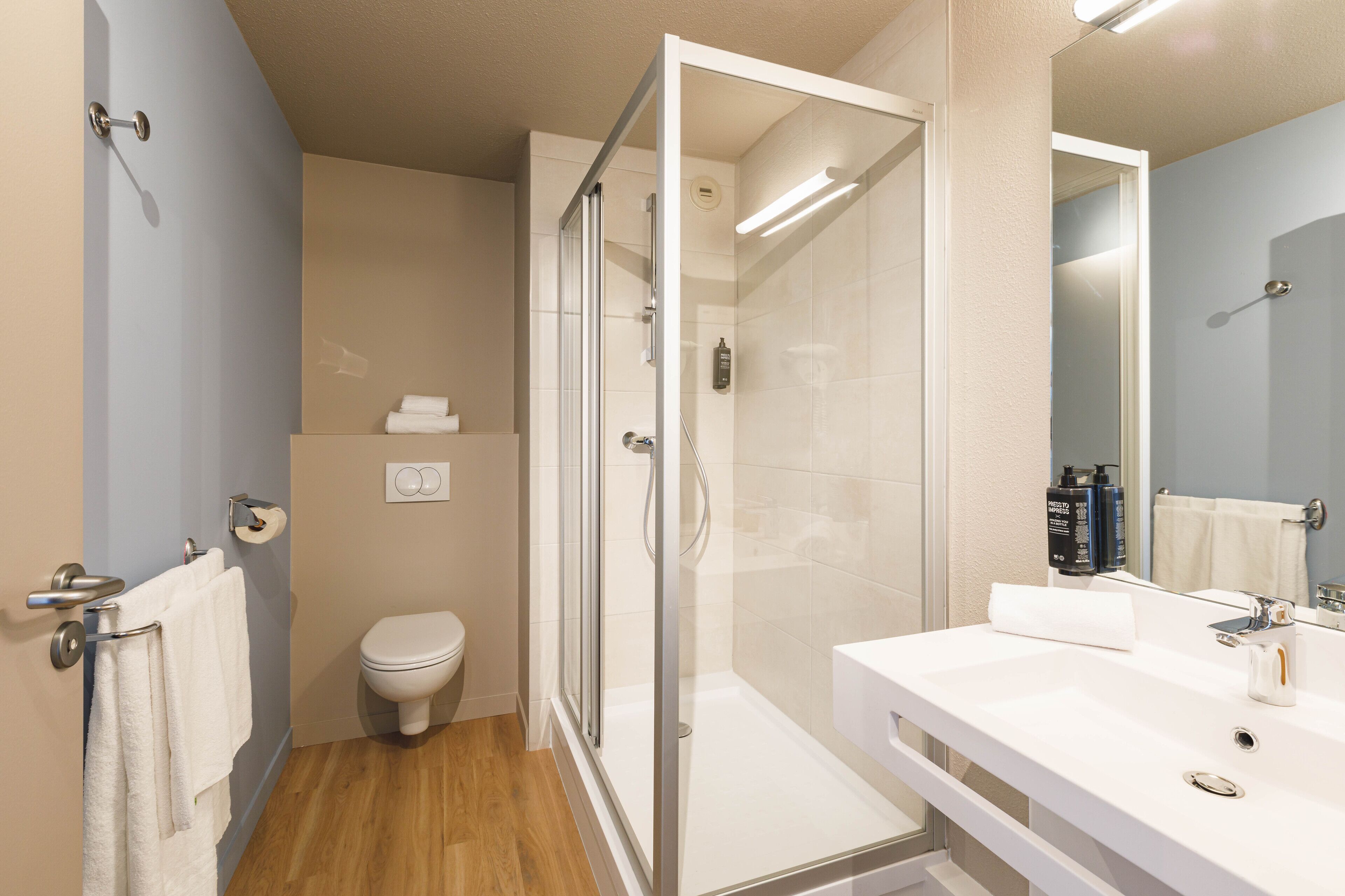 Un baño moderno con ducha envuelta en vidrio, un lavabo blanco y un inodoro.