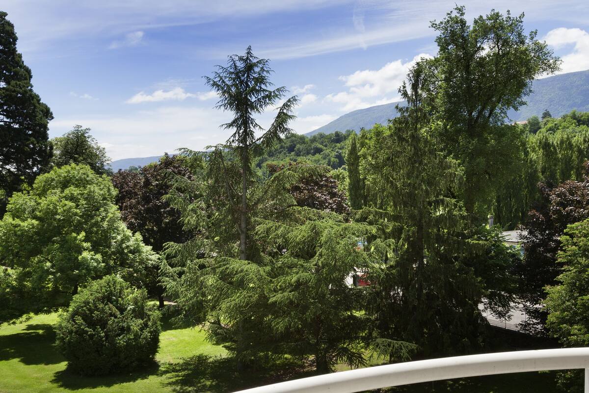 Un balcon avec piscine, une table à manger avec des produits pour le petit-déjeuner et une vue sur un jardin luxuriant et les montagnes.