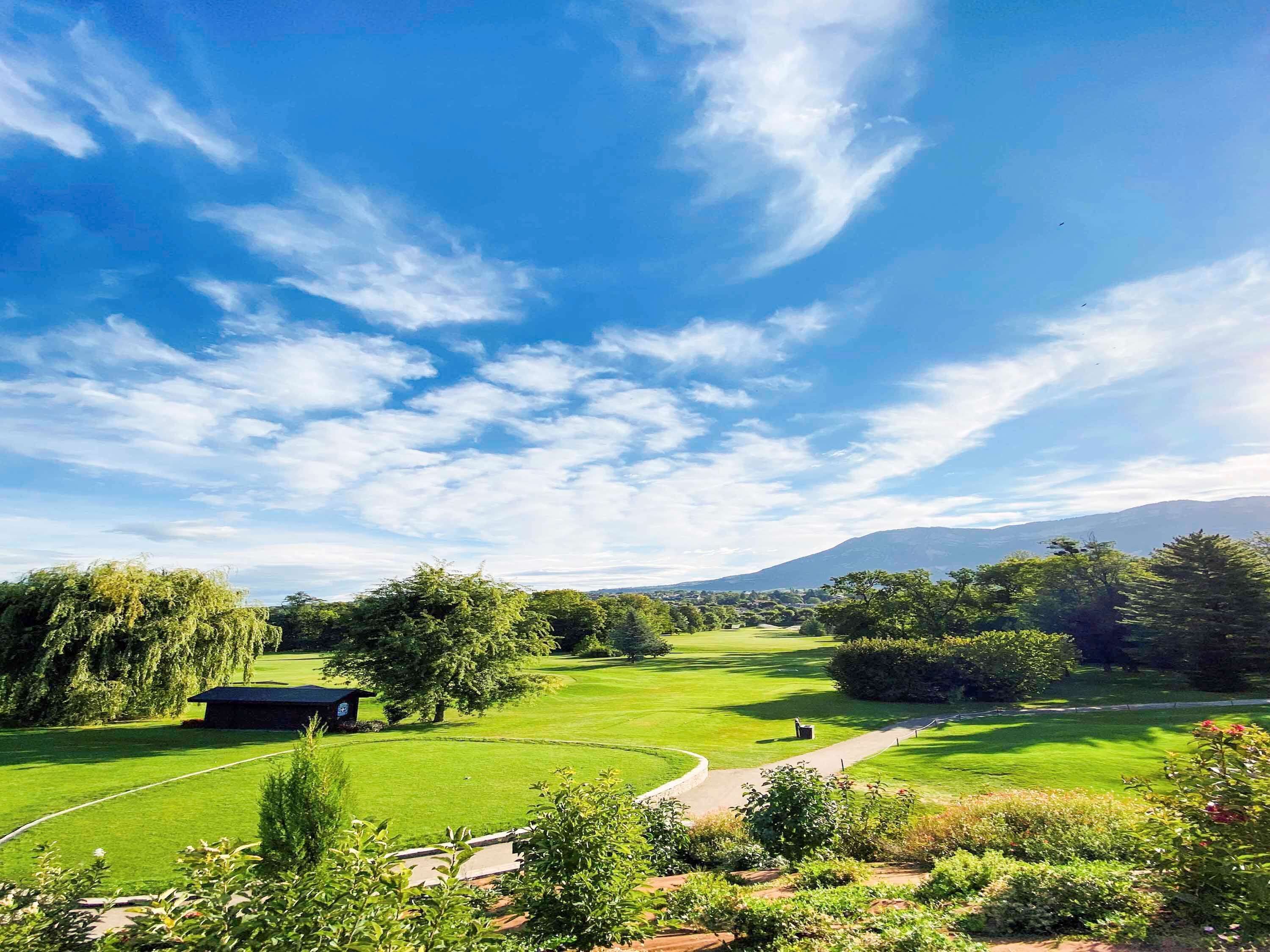 Un campo de golf con cielo despejado, abundante vegetación y una cadena montañosa distante.