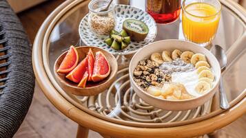A wicker chair with a tray table holding breakfast items including a bowl of cereal, sliced bananas, grapefruit, a glass of orange juice, and a jar of honey.