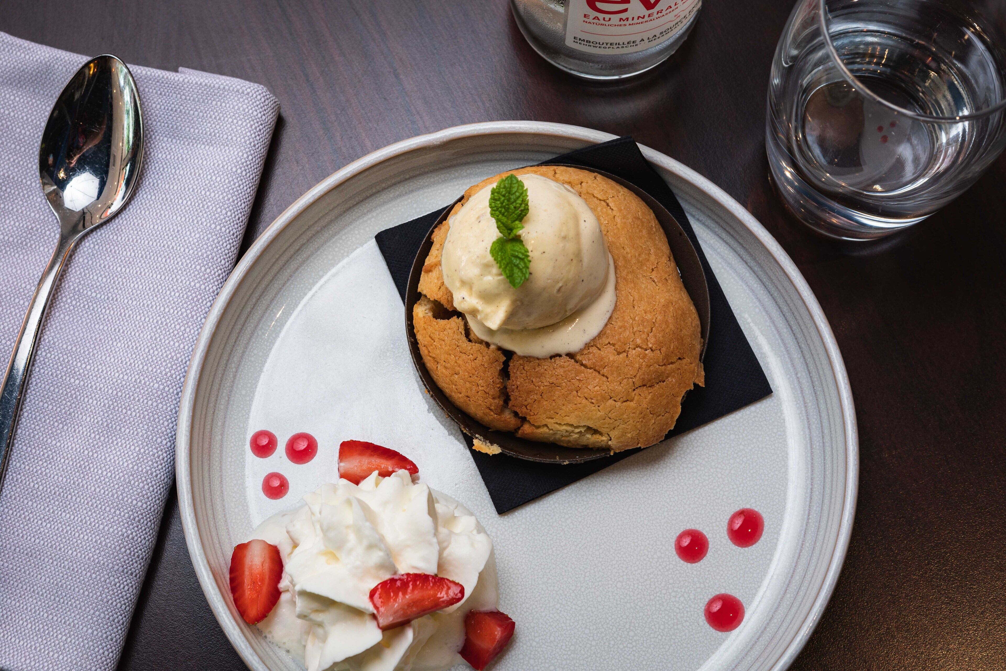 En desserttallrik med en kaka som är toppad med glass och ett myntablad, serverad med vispad grädde och jordgubbar.