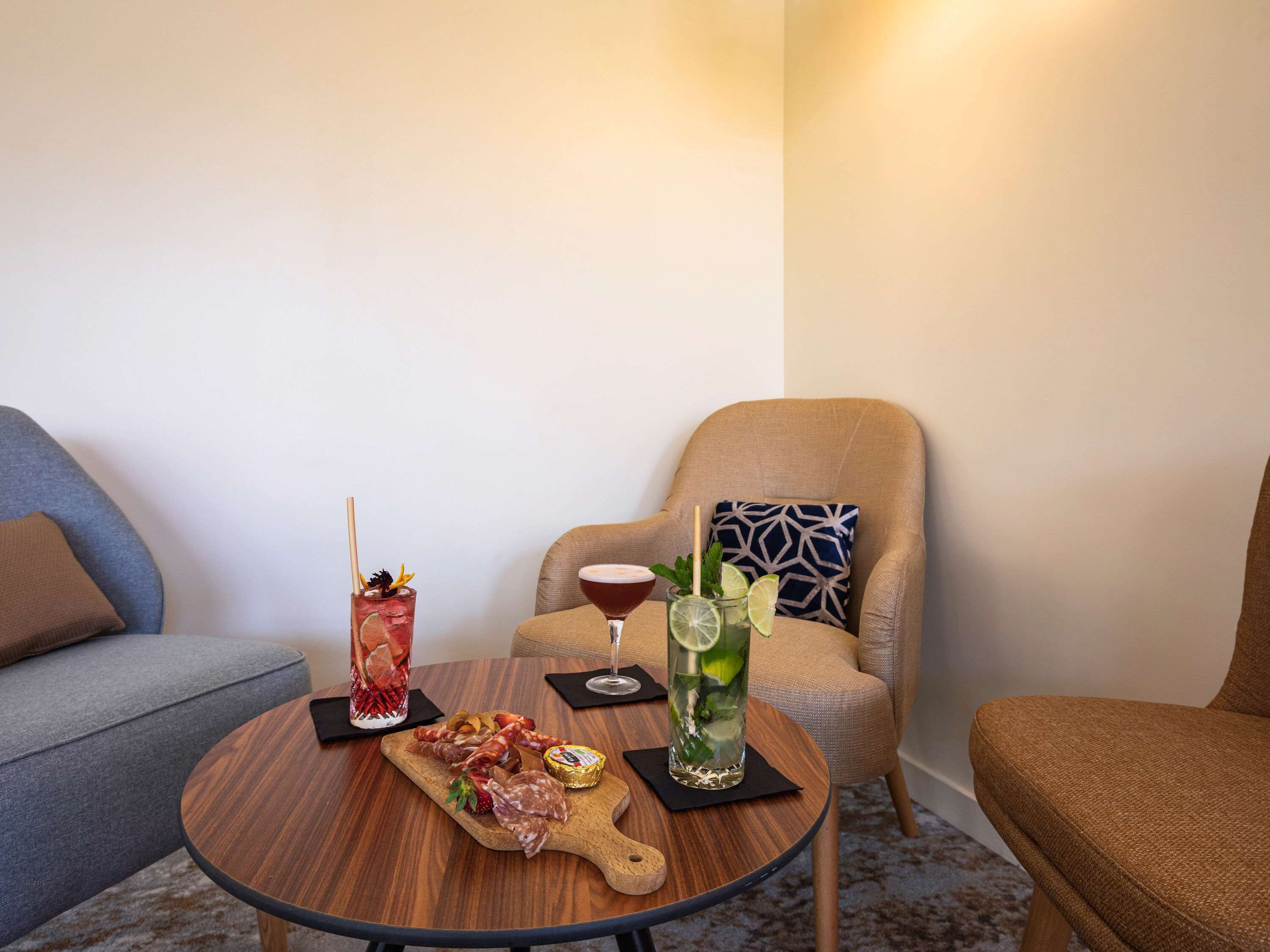 A small round table with a wooden board holding various meats, two drinks, and a glass of water.