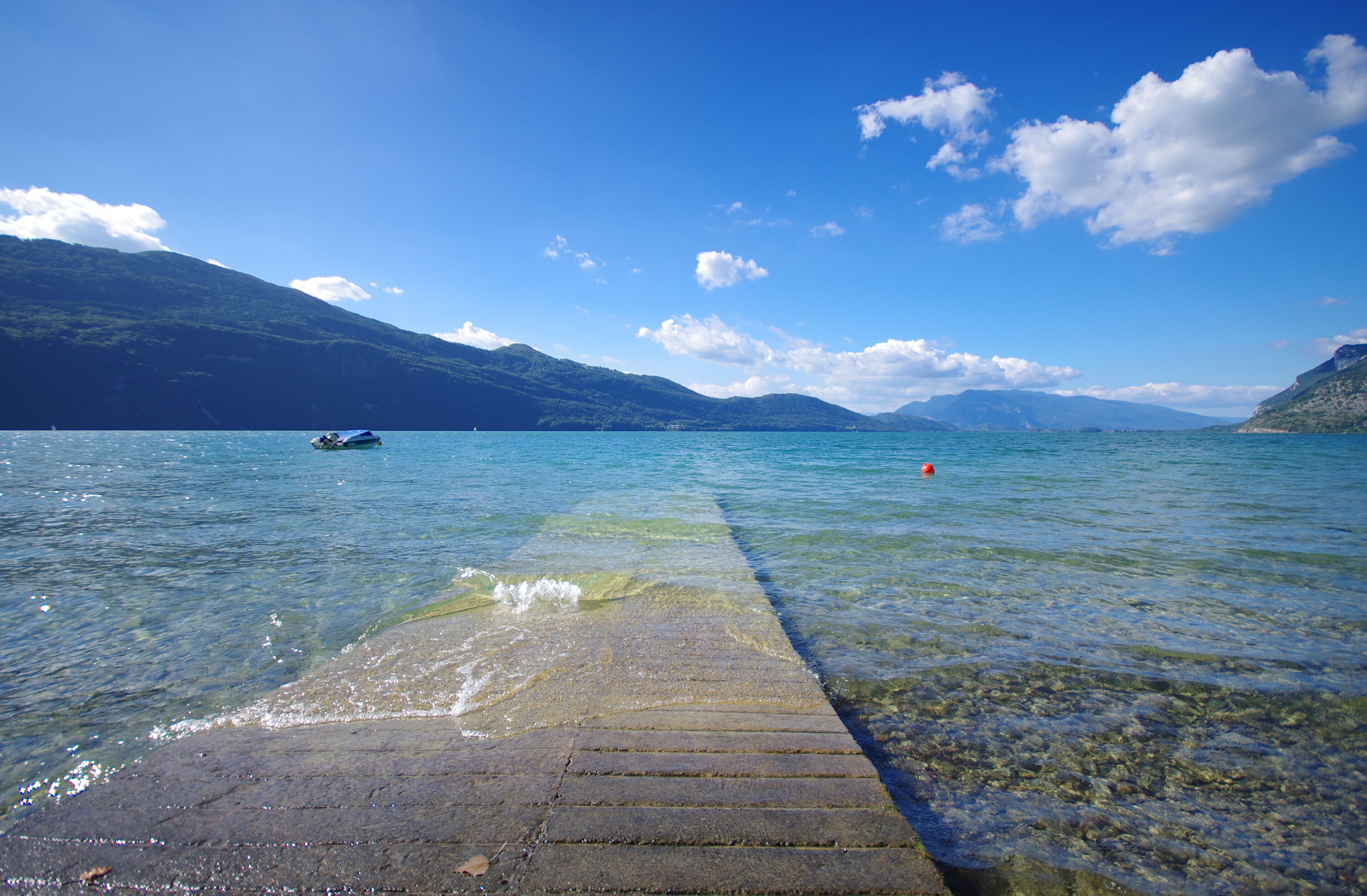 A clear lake with a dock extending into the water, surrounded by mountains and a clear sky.