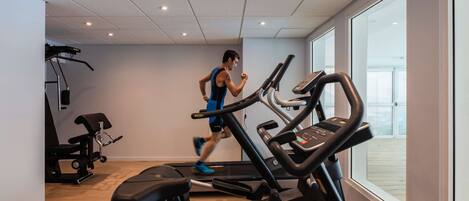 Un gimnasio con cintas de correr, una banca y una máquina de pesas.
