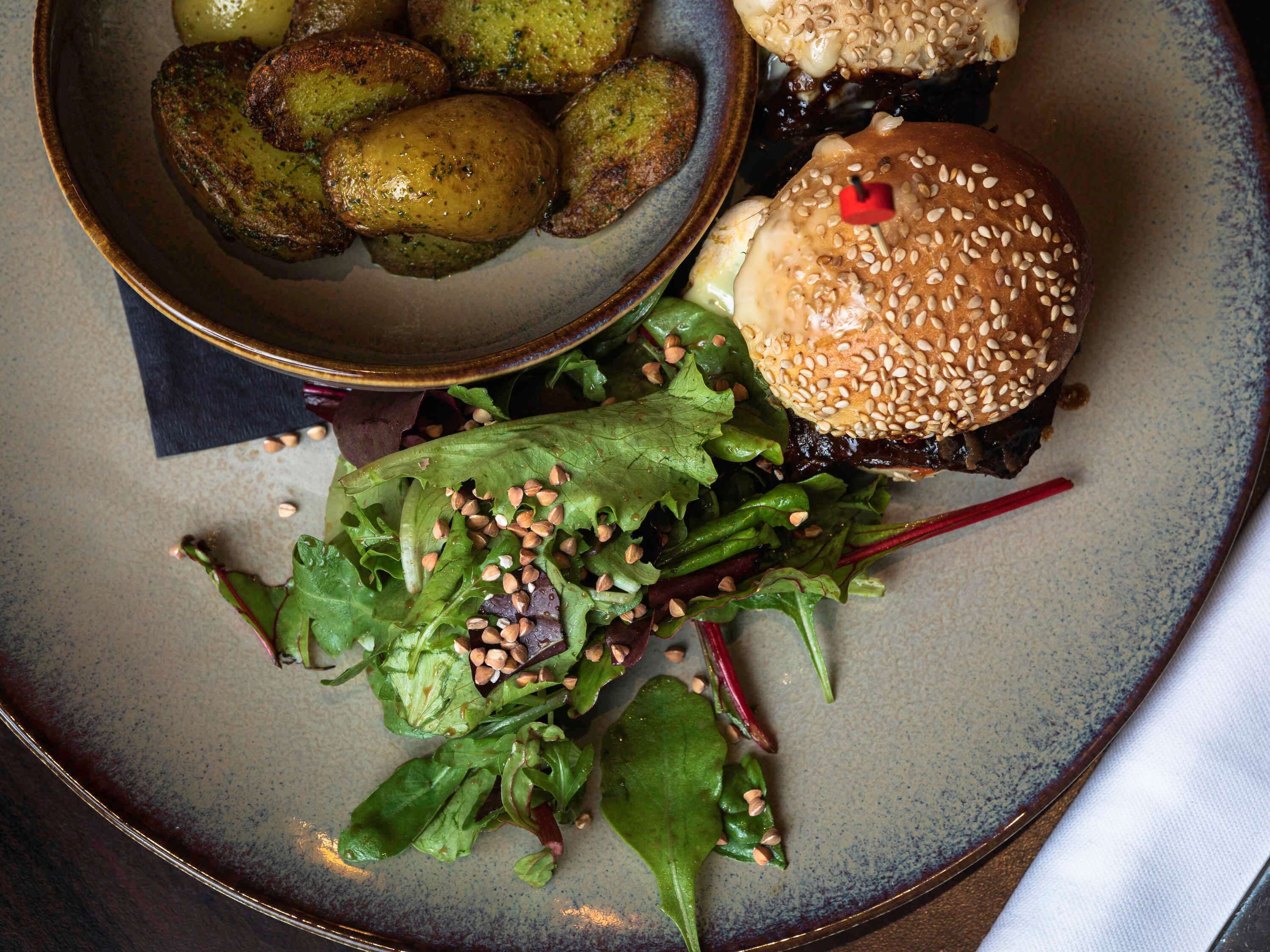 A plate with a burger, roasted potatoes, and a salad.