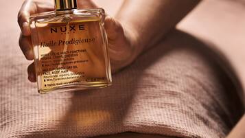 A person holding a bottle of Nuxe Huiles Prodigieuses.