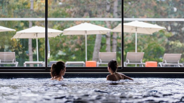 A hot tub area with two people, large windows, and outdoor seating with umbrellas. - Hotel Ibis Styles Aix-les-Bains Domaine de Marlioz (Aix-les-Bains)