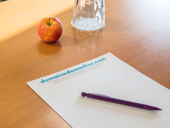 A wooden table with a paper displaying a website URL, a purple pen, and a glass of water.