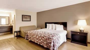 Une chambre d’hôtel comprenant un lit, une table de chevet avec une lampe, une chaise, un canapé, un bureau avec un miroir et un tableau encadré au mur.