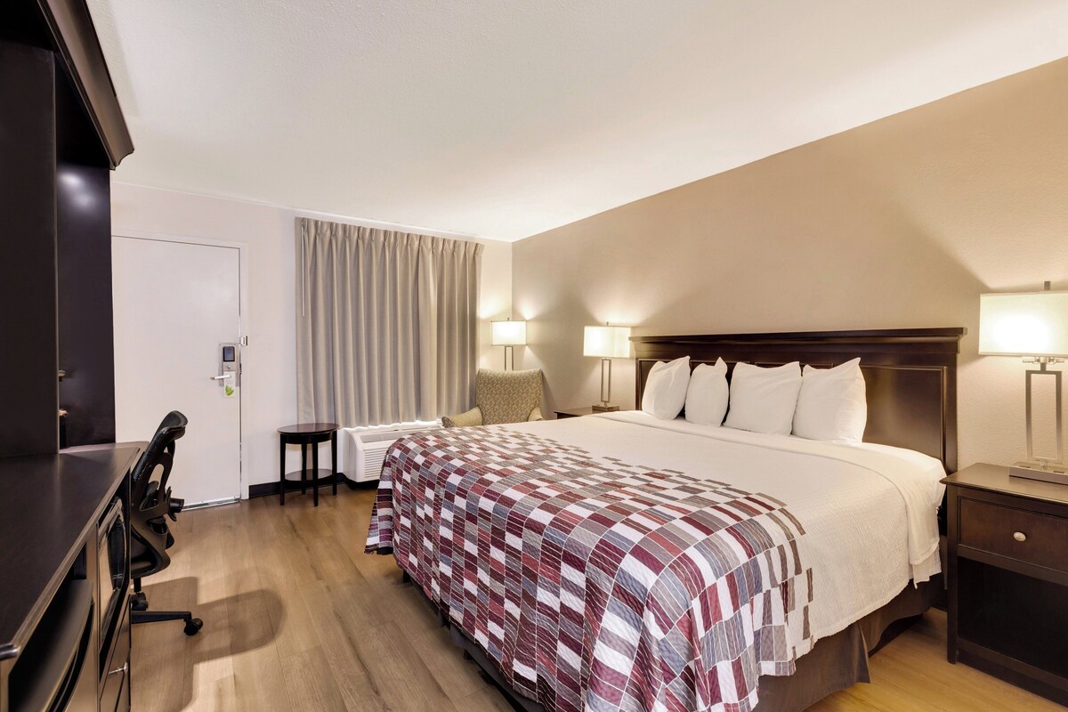 Ein Hotelzimmer mit einem großen Bett, zwei Nachttischen mit Lampen, einem Schreibtisch mit Stuhl und einer Tür mit Schloss.