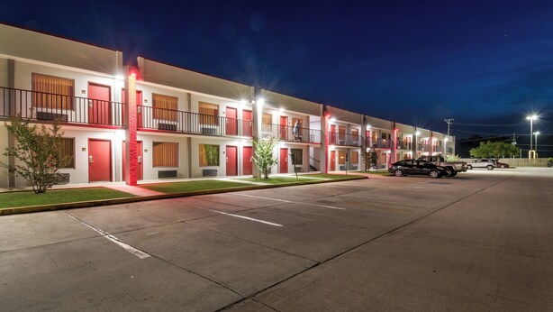 A multi-story motel with individual rooms, a parking lot, and a clear night sky.