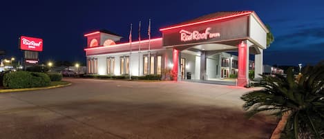 Un Red Roof Inn con un letrero grande, estacionamiento y una entrada bien iluminada.