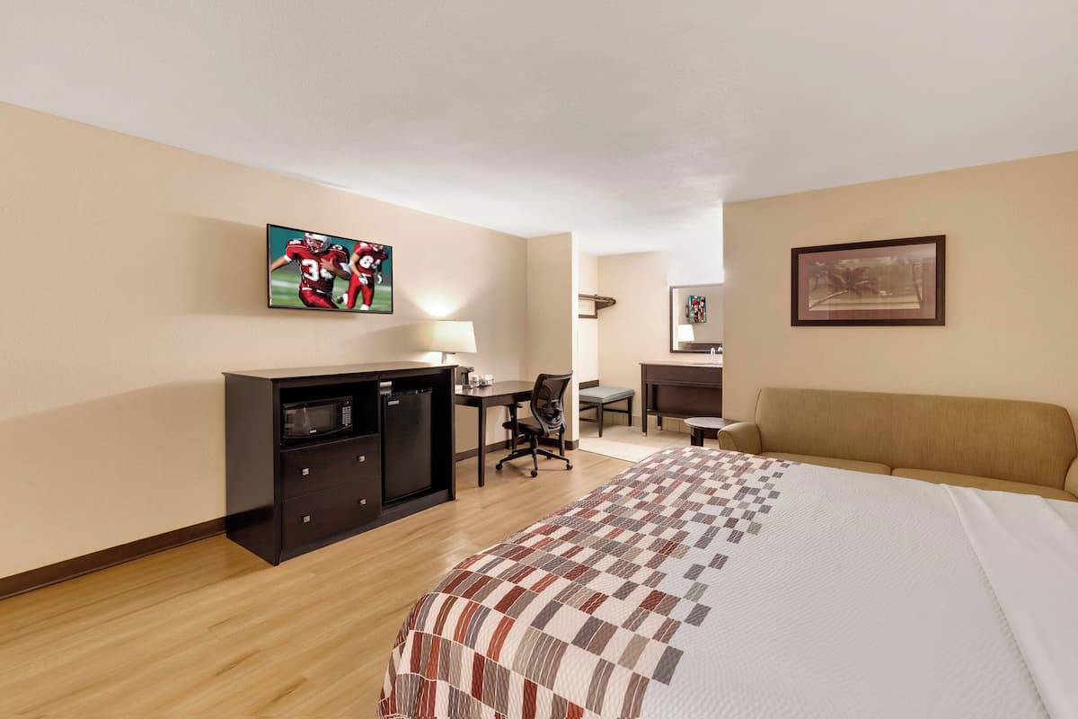 Ett hotellrum med en säng, ett skrivbord, en stol, en TV och en mikrovågsugn.