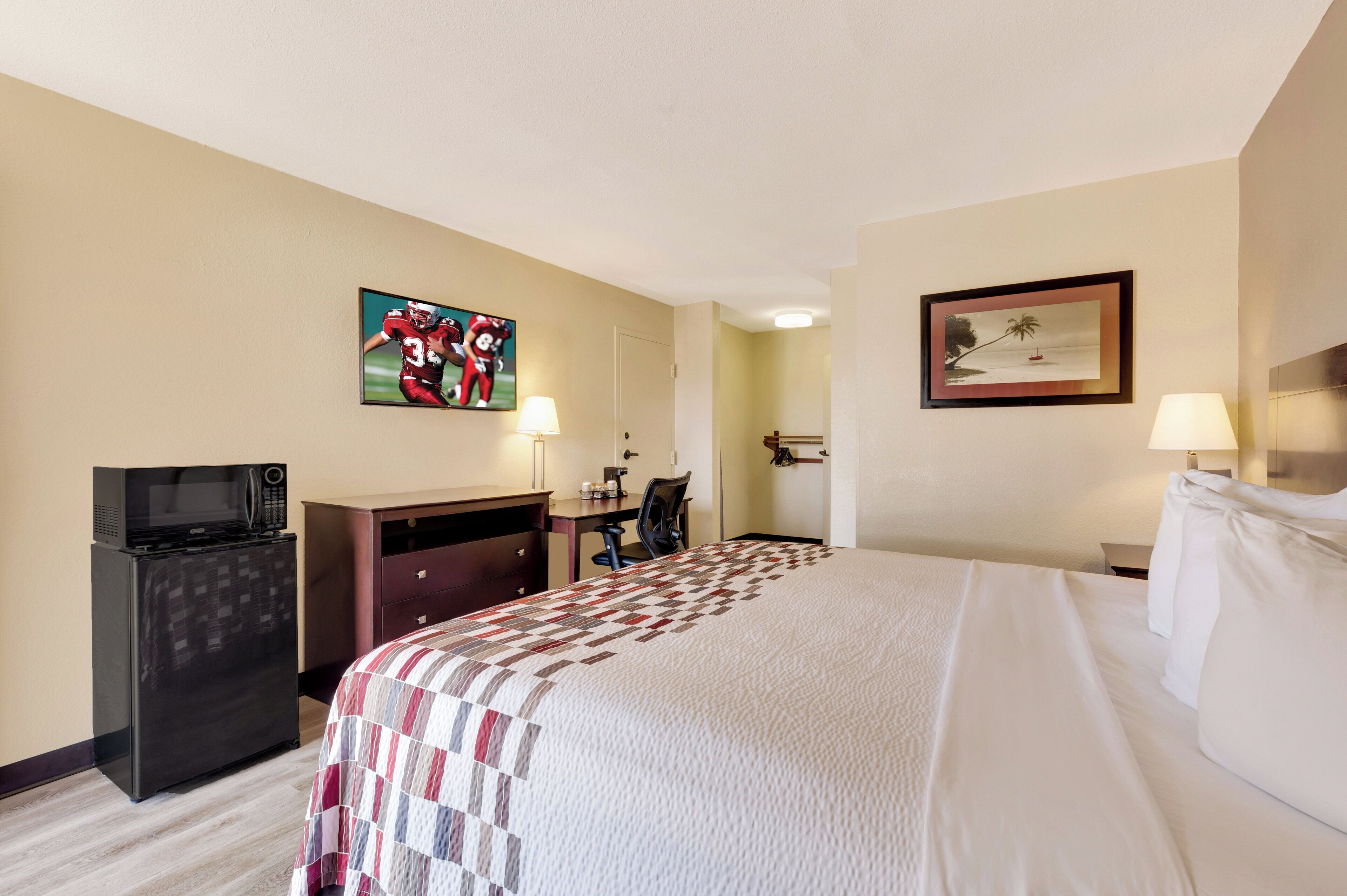 Een hotelkamer met een bed, een bureau met een computer, een televisie en een koelkast.