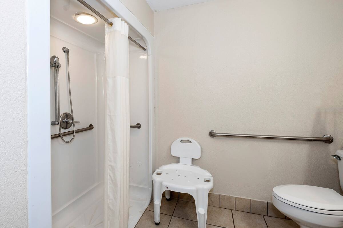 Ein Badezimmer mit Dusche, Toilette und einem kleinen weißen Kunststoffstuhl.