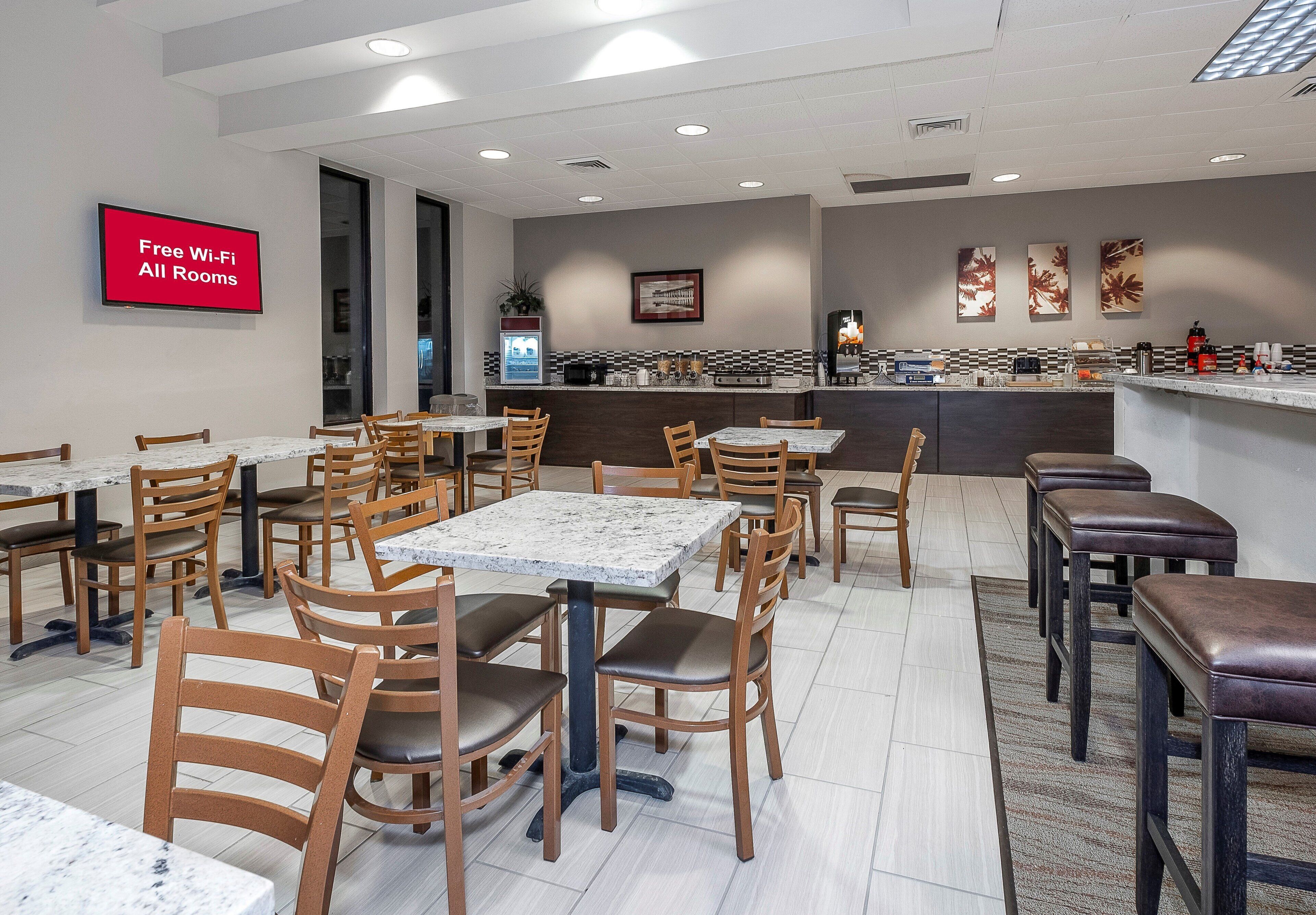 A restaurant with multiple tables and chairs, a kitchen area, and a sign indicating free Wi-Fi availability.