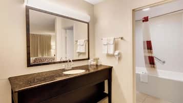 A bathroom with a dark countertop sink, a mirror, a towel rack, and a shower with a red towel.