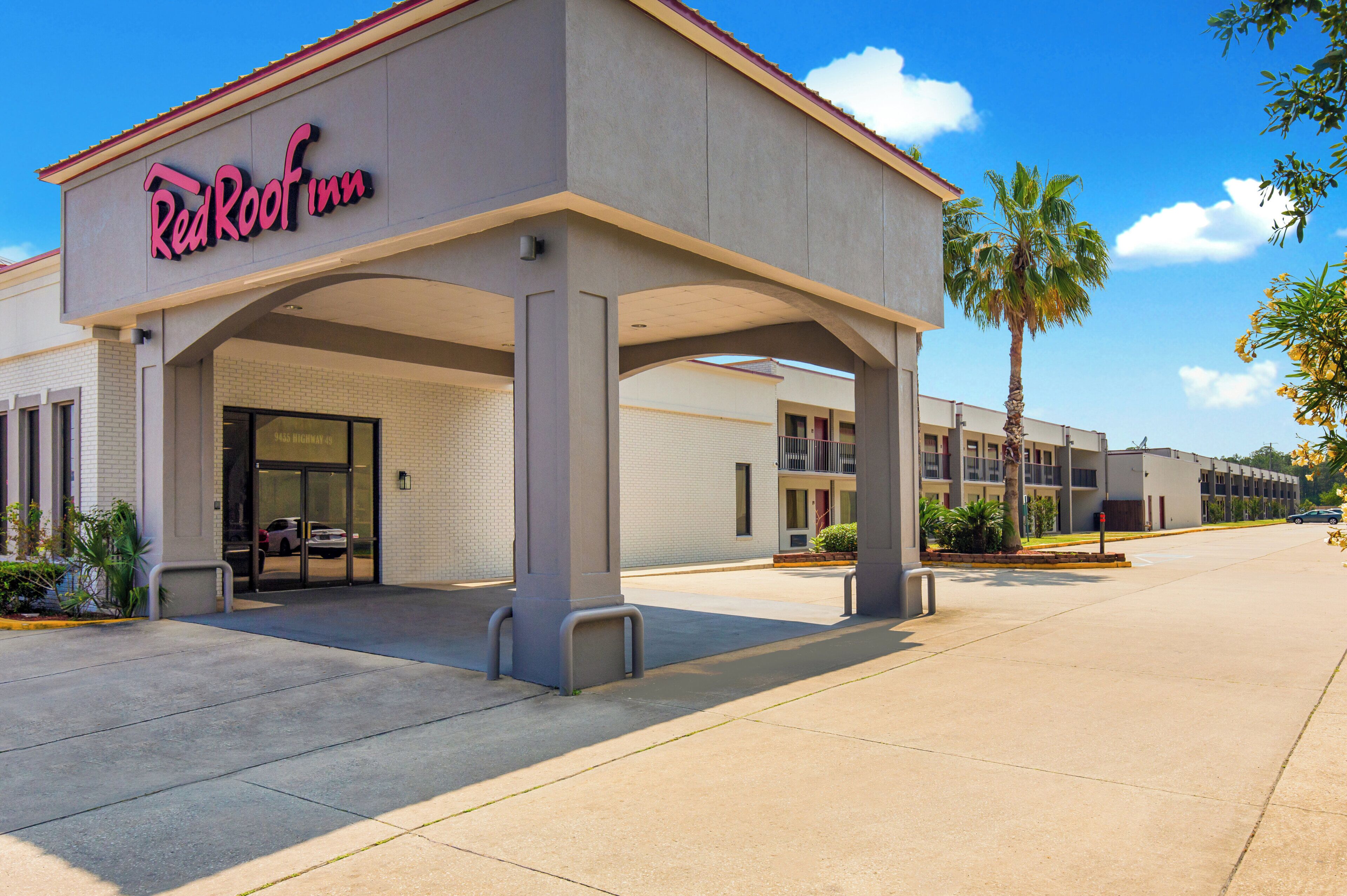 A hotel with a covered entrance, a parking lot, and a clear sky.