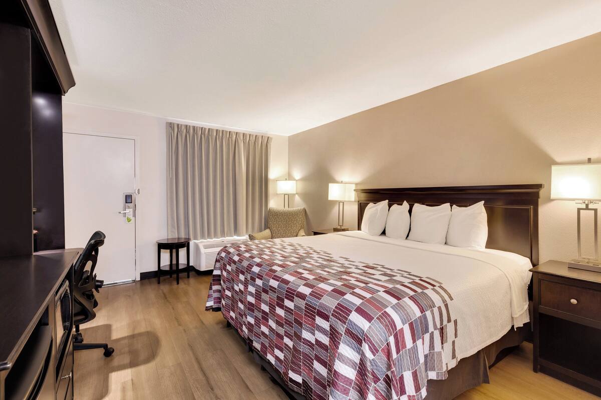 Ein Hotelzimmer mit einem großen Bett, zwei Nachttischen mit Lampen, einem Schreibtisch mit Stuhl und einer Tür mit Schloss.