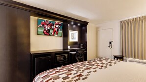 A hotel room with a large bed, a flat-screen TV mounted on the wall, a desk with a chair, and a door with a curtain.