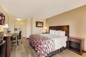 Ein Hotelzimmer mit Bett, Nachttisch, Lampe, Schreibtisch mit Stuhl und einem Fernseher.