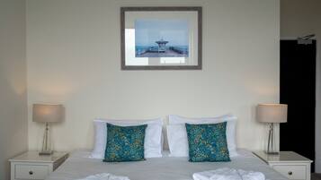 A neatly made bed with white linens and two decorative pillows, a framed picture above the bed, and two bedside lamps on white nightstands.