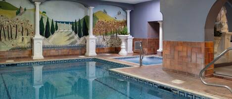 An indoor swimming pool with tiled walls, a mural, and classical architectural columns.