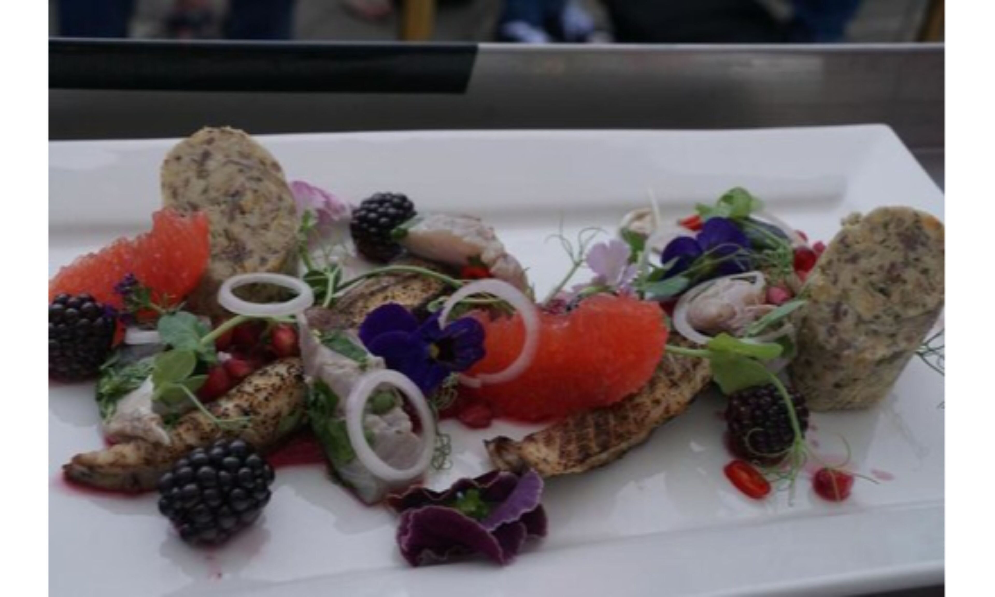 A white plate with a variety of food items including fish roe, blackberries, and greens.