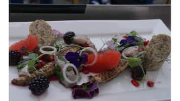 A white plate with a variety of food items including fish roe, blackberries, and greens.