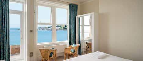 Habitación de hotel con cama, dos sillones de mimbre, un escritorio y vista al mar.