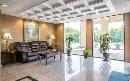 A lobby with a leather sofa, two lamps, a painting, and potted plants.